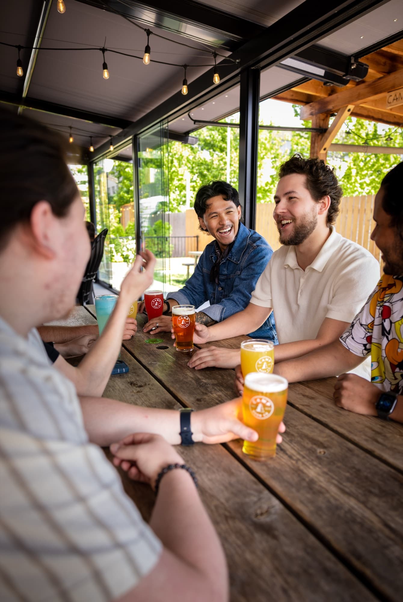 Friends laughing over colourful Camp Beer Co. pints at a patio picnic table